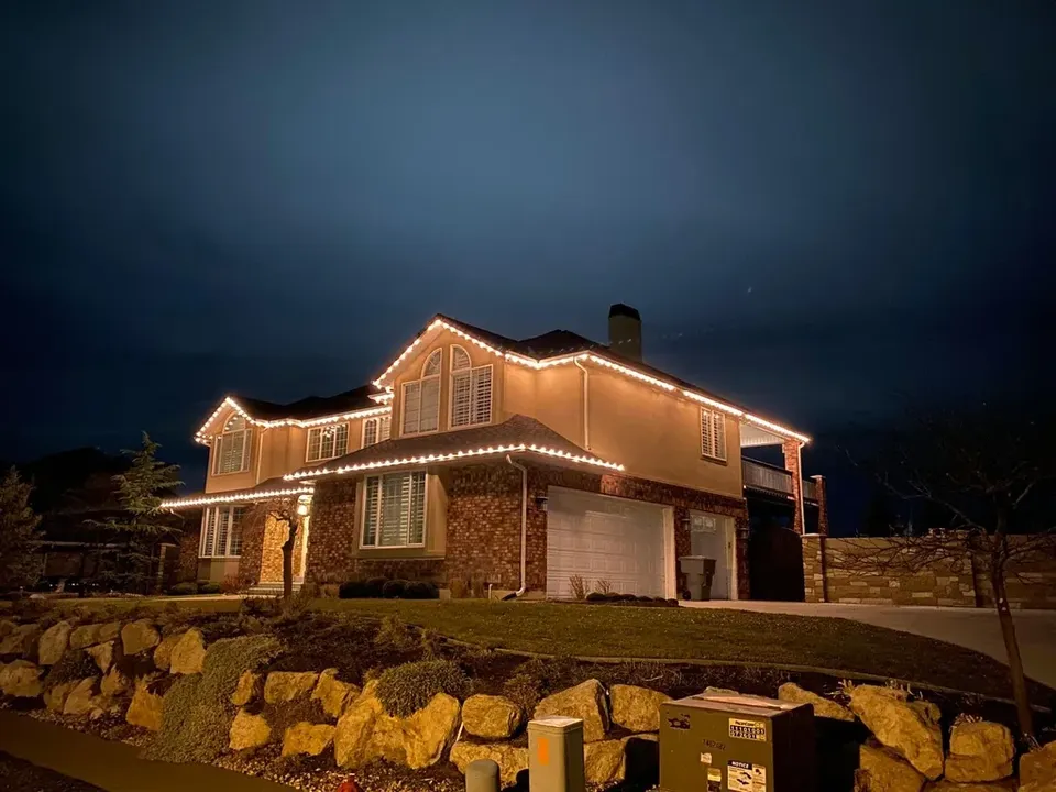 Corner view of a two-story home lit in warm white along every roofline